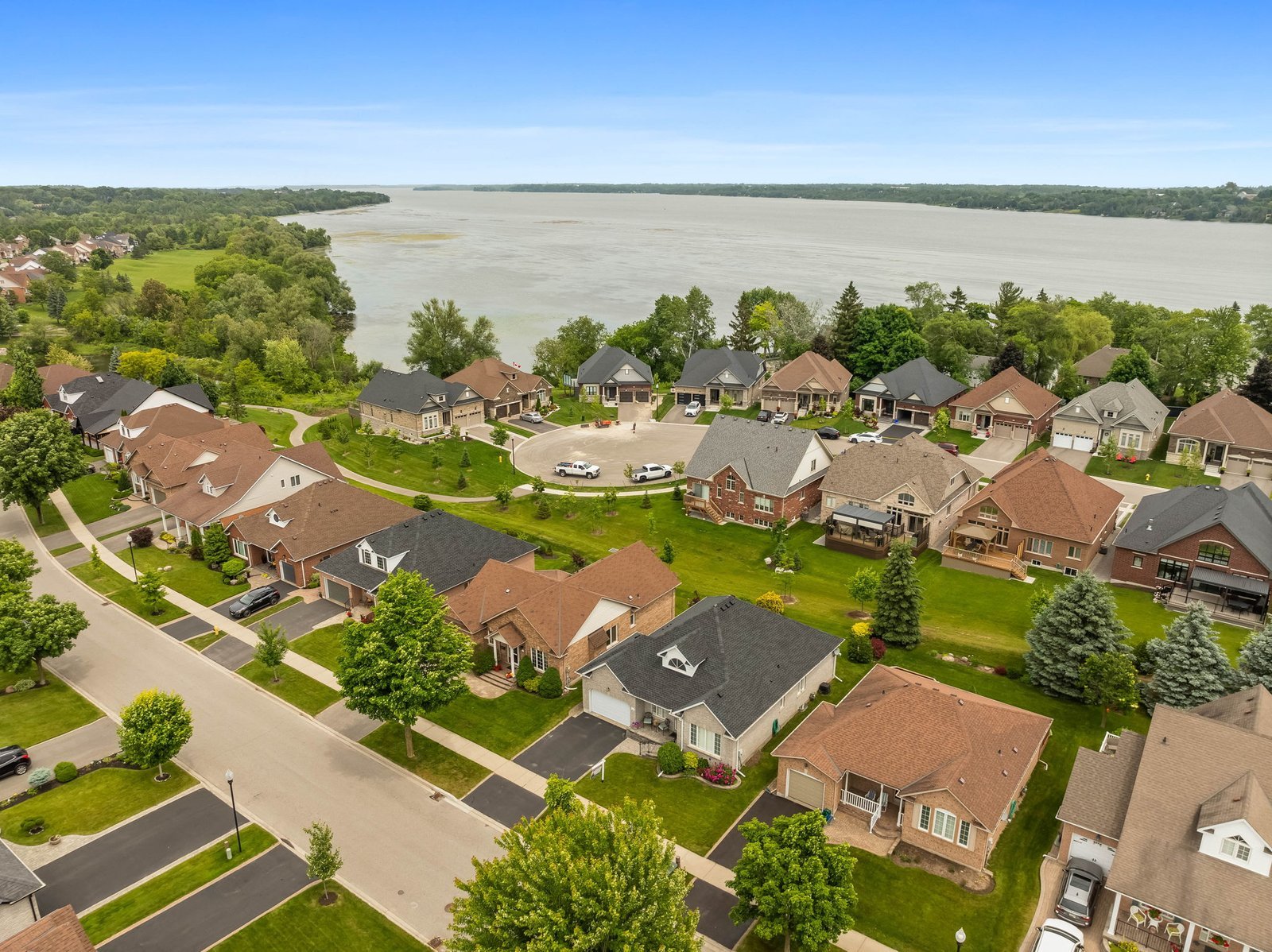 Aerial view of a suburban neighborhood with rows of houses, tree-lined streets, and a large lake in the background.