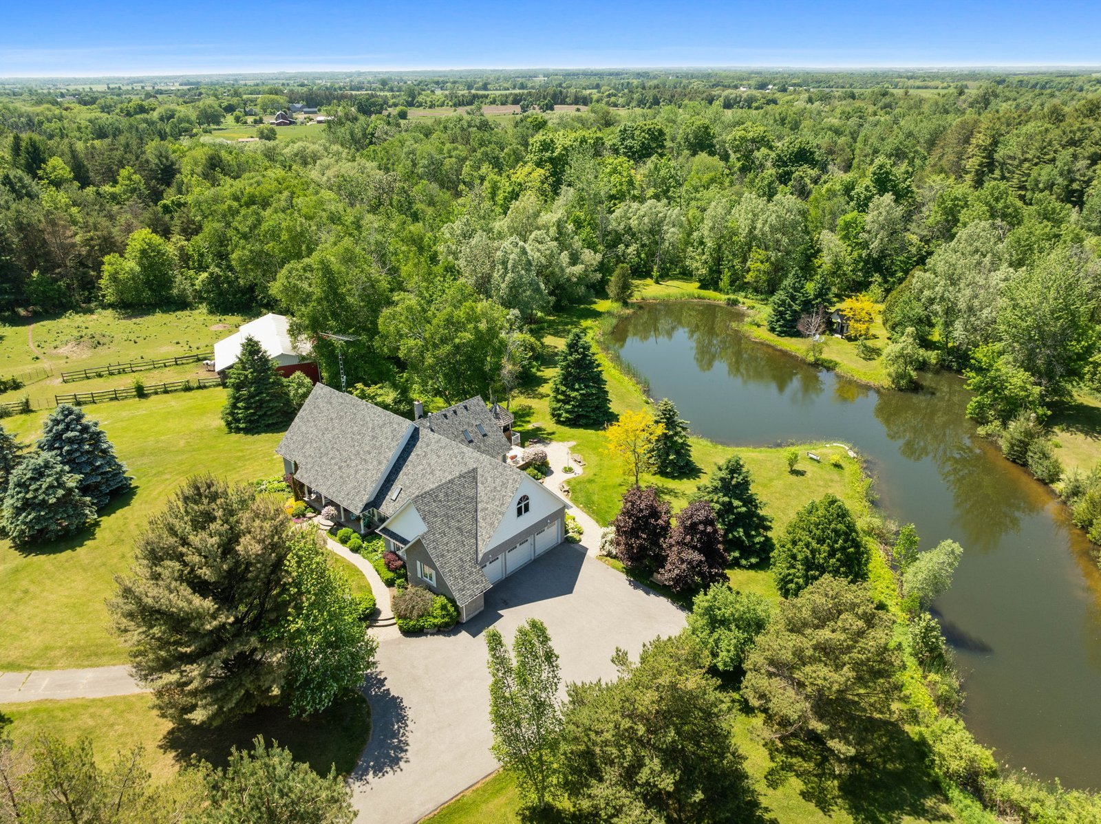 Aerial view of a large country house with a pond, surrounded by trees, lawns, and open green fields under a clear blue sky.