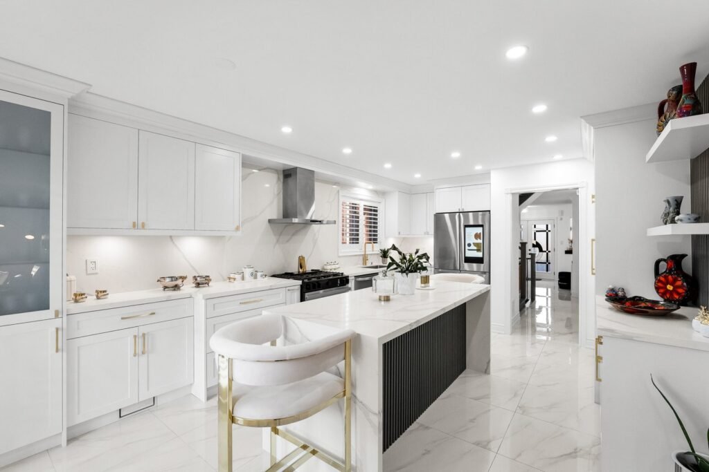 Modern kitchen with white cabinets, marble countertops, center island with seating, stainless steel appliances, and bright recessed lighting.