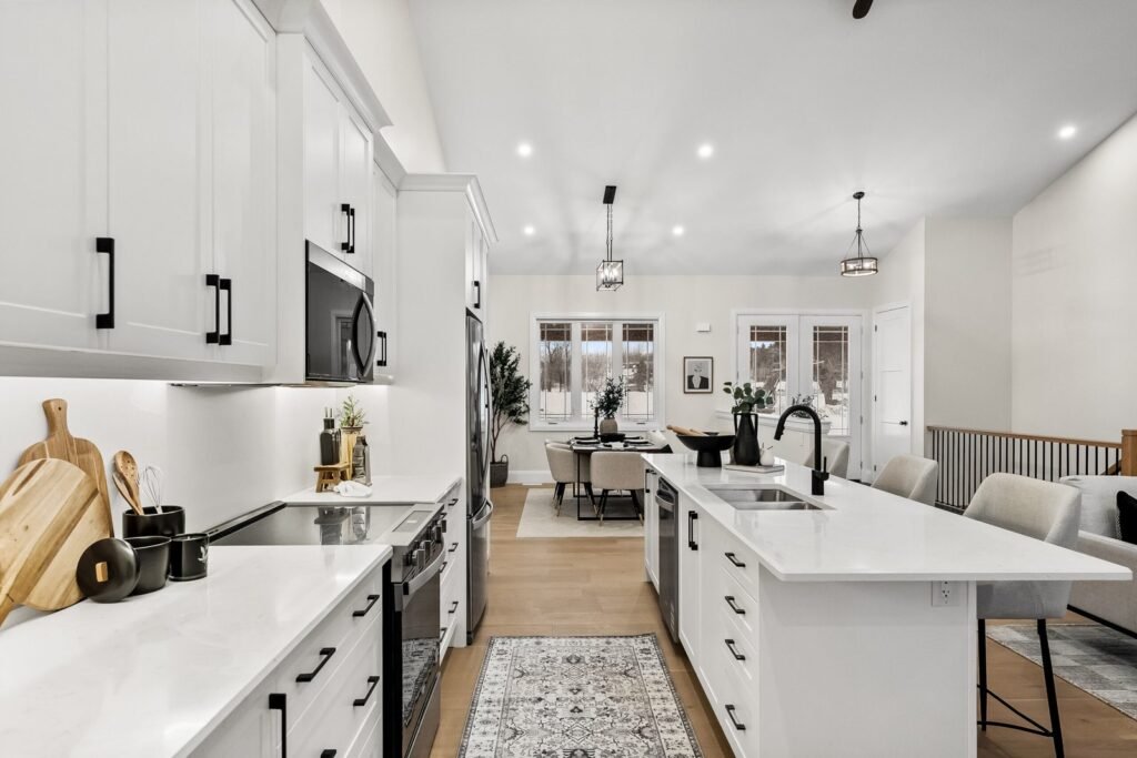 Modern kitchen with white cabinets, black hardware, marble countertops, an island with stools, and a view into the dining area and living space.