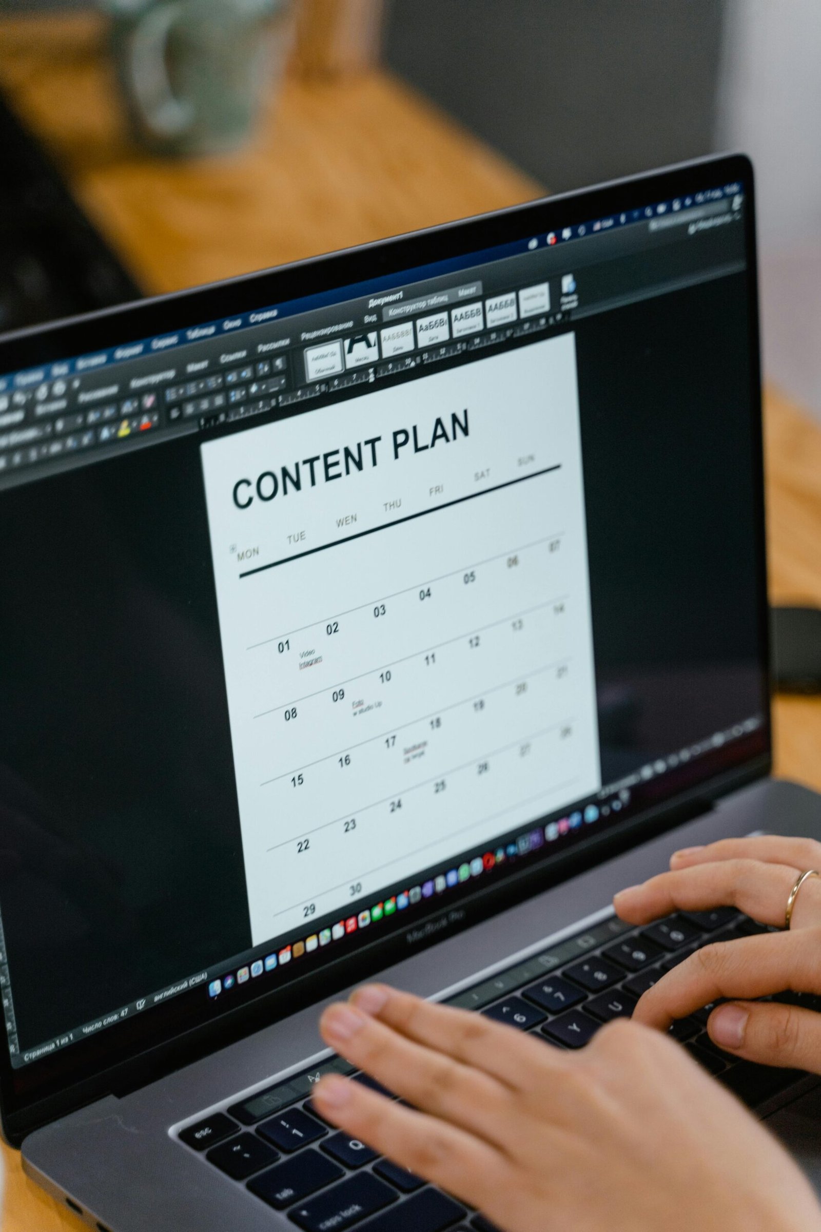 A person types on a laptop displaying a document titled "Content Plan" with a calendar layout on the screen.