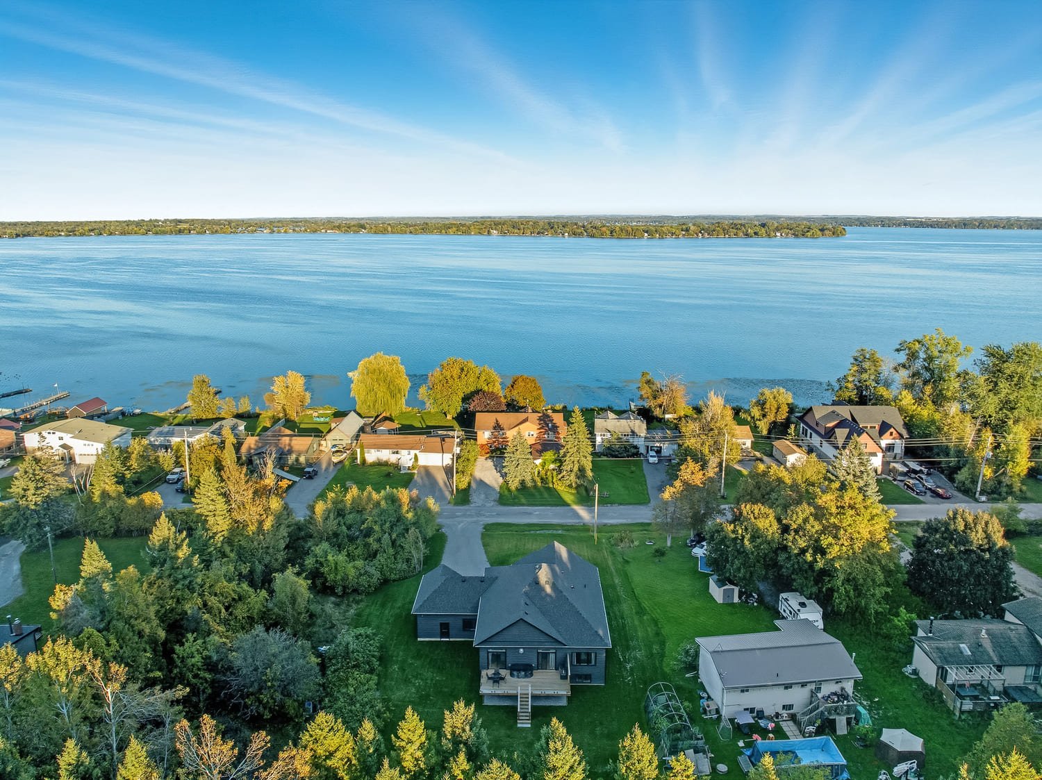 Aerial view of lakeside homes surrounded by trees, with a wide expanse of calm blue water and distant shoreline under a clear sky.